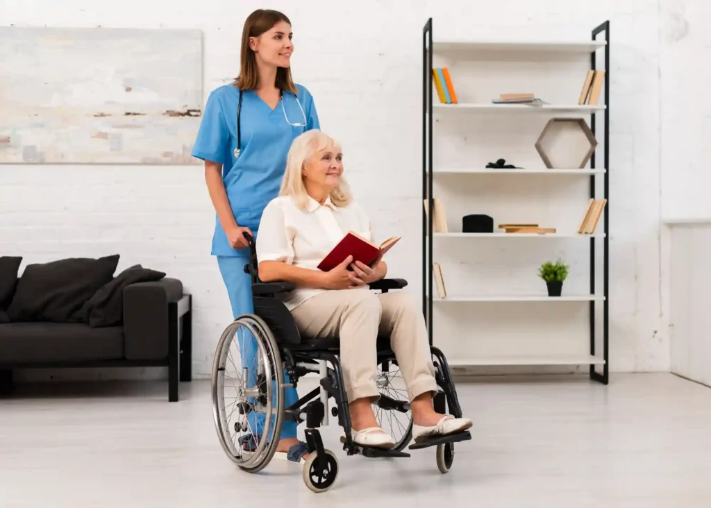 A woman in a wheelchair is accompanied by a nurse standing beside her, both engaged in conversation.