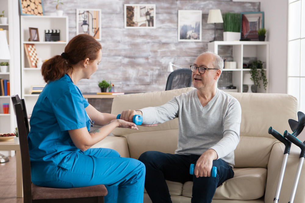 A man and woman sit together on a couch, with a cane resting beside them, sharing a moment of conversation.