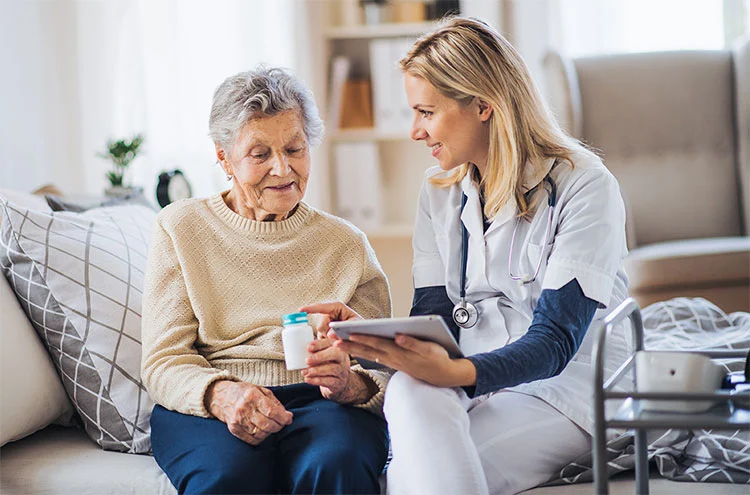 A nurse and an elderly woman relax on a couch, enjoying each other's company in a cozy setting.